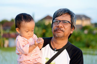 Portrait of smiling grandfather and grandchild standing outdoors