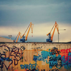 Low angle view of cranes at harbor against cloudy sky