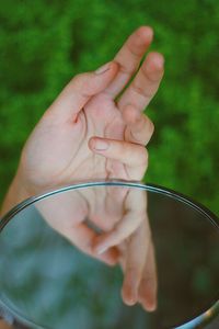 Cropped hand reflecting in mirror against plants