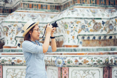 Woman photographing with camera against historic building