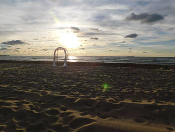 A wedding arch sits on an empty beach in front of the setting sun