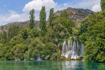 Scenic view of waterfall by lake against sky