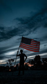 Silhouette man holing flag against sky