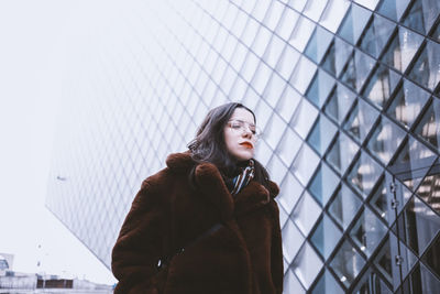 Young woman standing against sky in city