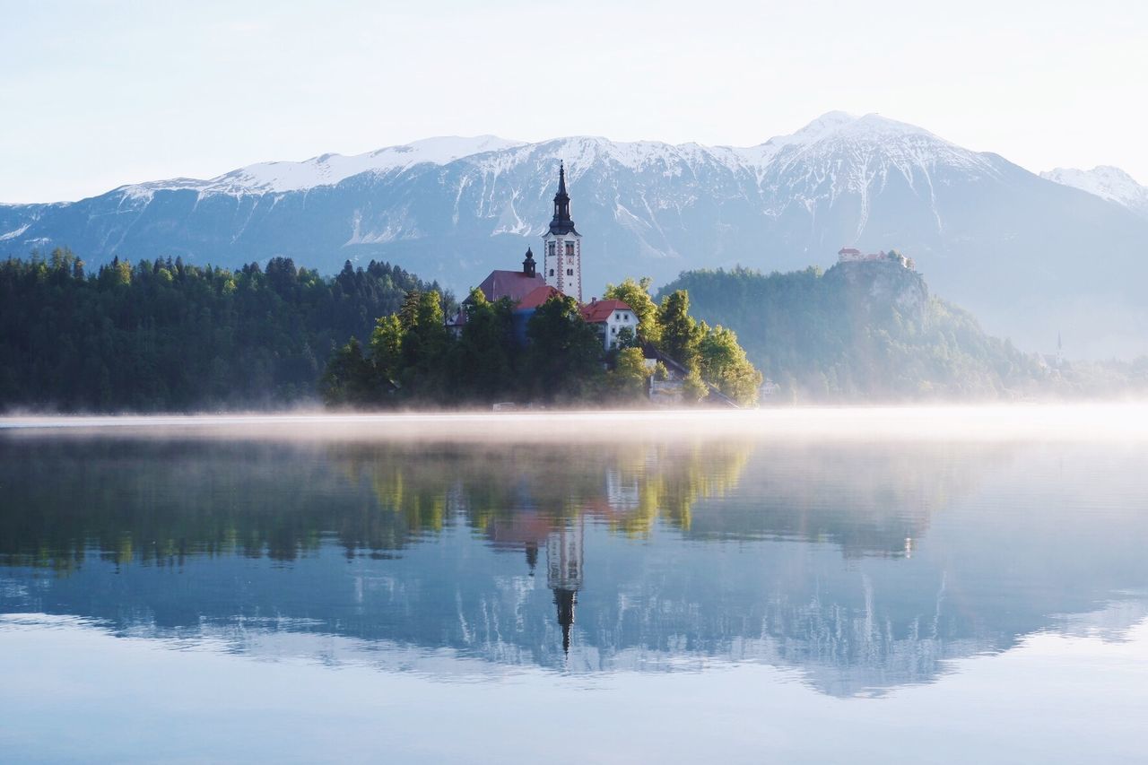 mountain, water, beauty in nature, reflection, lake, scenics - nature, sky, religion, mountain range, spirituality, architecture, built structure, nature, building exterior, place of worship, waterfront, day, belief, no people, outdoors, snowcapped mountain