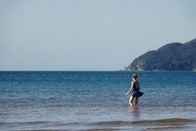 Young woman walking into sea  against clear sky