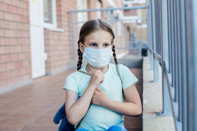 Close-up of cute girl wearing mask standing by building