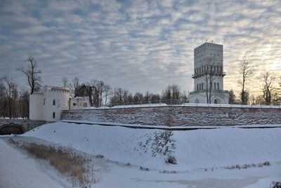 Snow covered field by building against sky