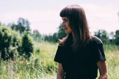 Young woman looking away while standing on field against sky