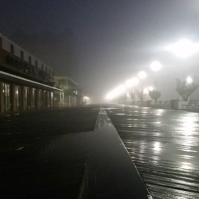 illuminated, night, the way forward, water, street light, diminishing perspective, built structure, architecture, lighting equipment, reflection, vanishing point, sky, transportation, building exterior, light - natural phenomenon, connection, outdoors, bridge - man made structure, railing, river