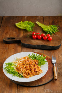 A plate of pasta in bolognese sauce on a nearby fork and cherry tomatoes on a board. vertical photo