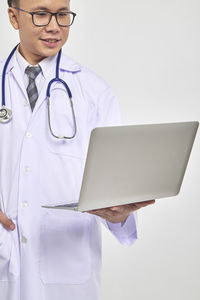 Portrait of smiling doctor holding laptop against white background