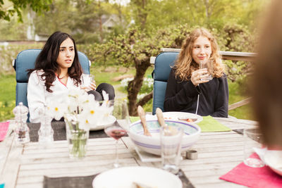 Teenage girls looking away while sitting at outdoor table in yard