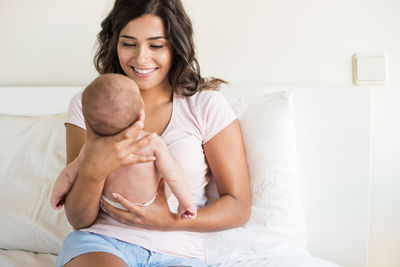 Happy mother with baby sitting on sofa