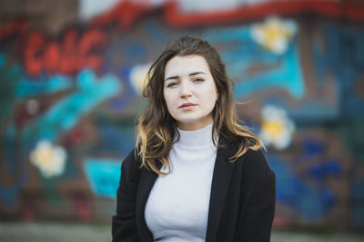 Portrait of beautiful young woman standing against graffiti