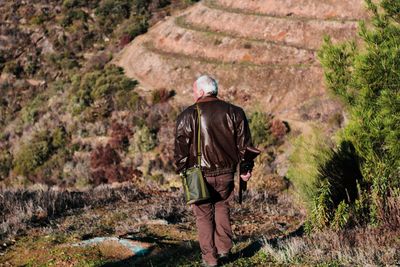 Rear view of man with rifle walking on field