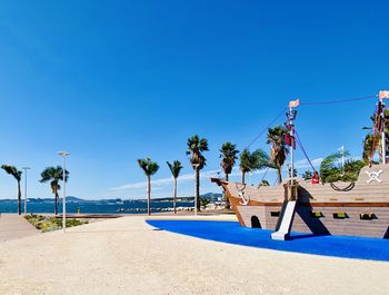 Palm trees by swimming pool against clear blue sky