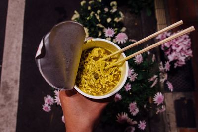 Cropped image of person holding instant noodles against flowers at night