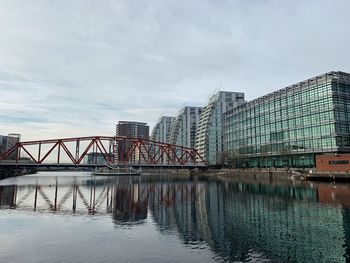 Bridge over river by buildings against sky