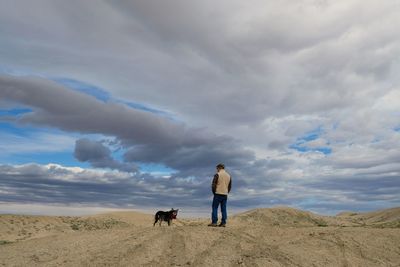 Rear view of man with dog standing at desert