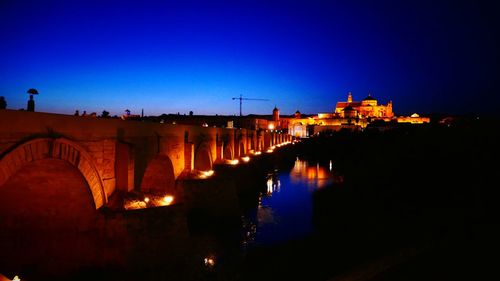 Illuminated bridge over river against blue sky at night