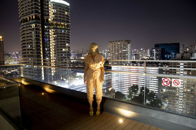 Full length of woman wearing headscarf standing on building terrace at night