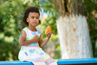 Girl eating food while sitting on bench against plants