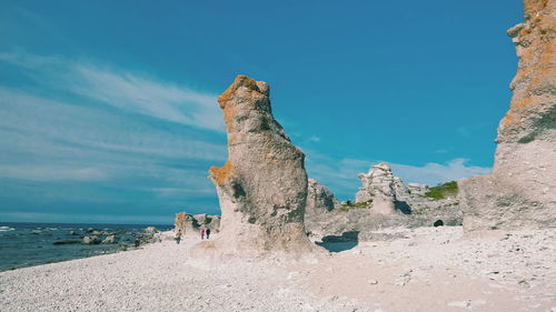 Low angle view of rock formations at beach against blue sky on sunny day