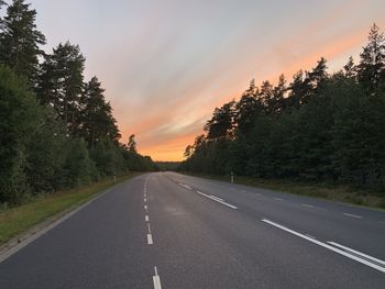 Road by trees against sky during sunset