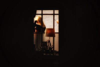 Rear view of silhouette woman standing by window at home