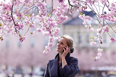 Young woman with cell phone near cherry blossom trees