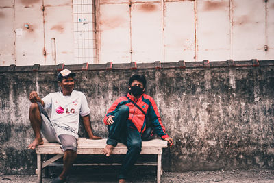 People sitting on bench against wall