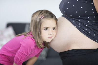 Close-up of daughter listening to pregnant mother belly at home