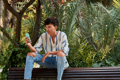 A young man with afro hair watching his smartphone sitting on a bench