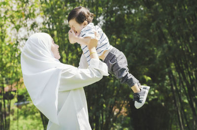 Side view of mother playing with son against trees