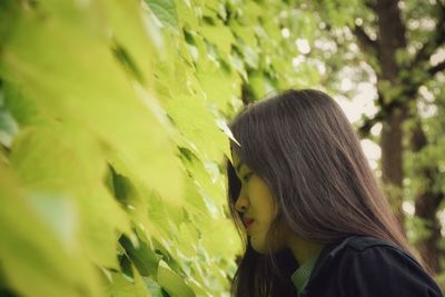 Side view of woman looking at plants while standing in park