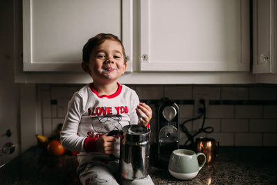 Young boy sitting on kitchen counter with frothed milk on face