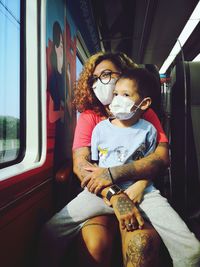 Portrait of woman and her son sitting in train with mask