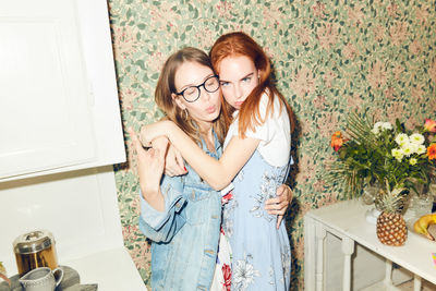 Portrait of young redhead woman embracing female friend showing horn sign at home