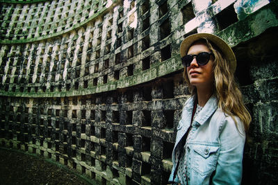 Young woman in sunglasses standing against patterned wall