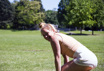 Side view of woman bending while standing on field at park