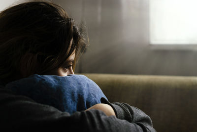 Close-up of sad woman hugging cushion while sitting at home