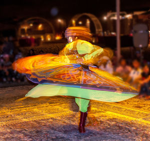 Rear view of woman walking on illuminated street at night