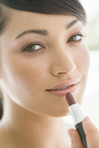 Close-up portrait of beautiful woman applying lipstick on lips