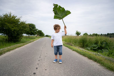 Rear view of boy standing on road against sky