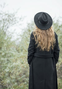 Portrait of young attractive woman in black coat and hat. autumn landscape, dry grass. back view