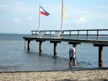 Rear view of man standing by sea against sky