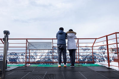 Rear view of people standing on railing against sky