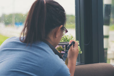 Rear view of woman holding camera against window