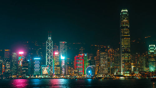 Illuminated buildings by river against sky at night